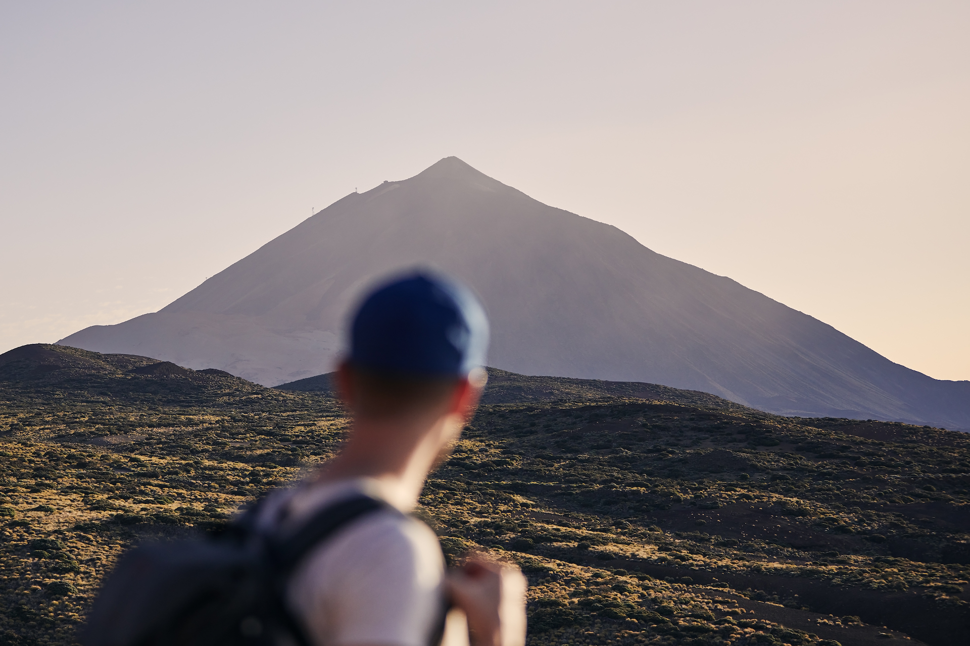 Traveler against landscape with Pico de Teide at dusk. Young man with backpack looking on volcano. Tenerife, Canary Islands, Spain.