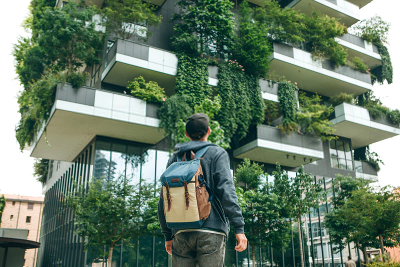 Étudiant avec un sac à dos regardant un bâtiment contemporain à façade végétalisée, reflétant l'engagement du Bachelor Tourisme de l'Institut Atlas pour l'innovation durable et l'architecture verte dans l'industrie du voyage.